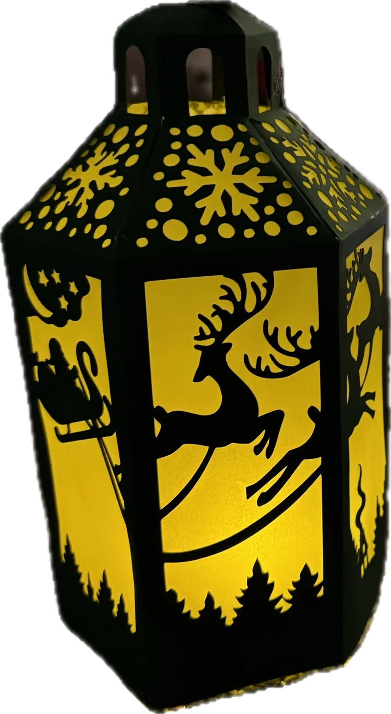 A black cut-paper lantern lit from inside, showing a reindeer and sleigh in silhouette against a warm glow.