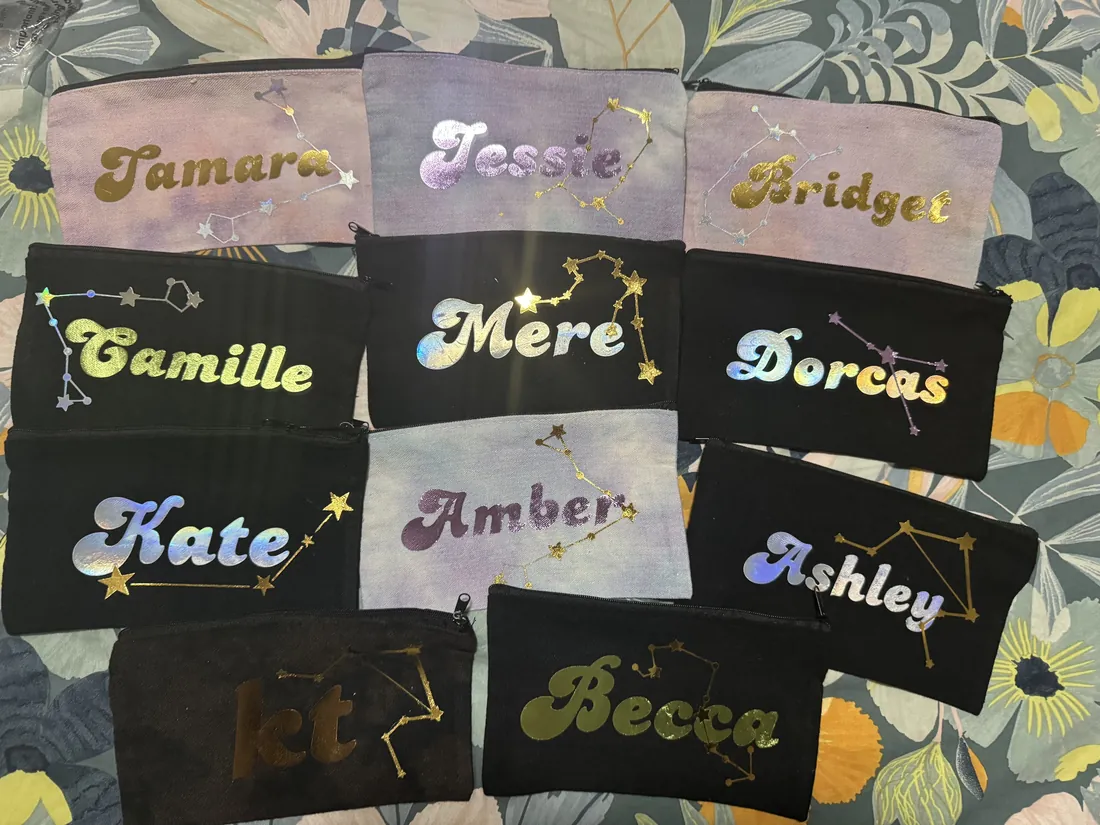 Eleven zip pouches laid out together, each printed with a different first name and that person's star constellation.