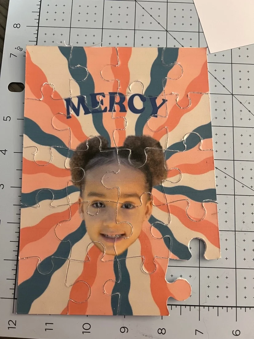 A custom jigsaw puzzle with an orange and blue sunburst design, a name across the top and a child's photograph in the middle.